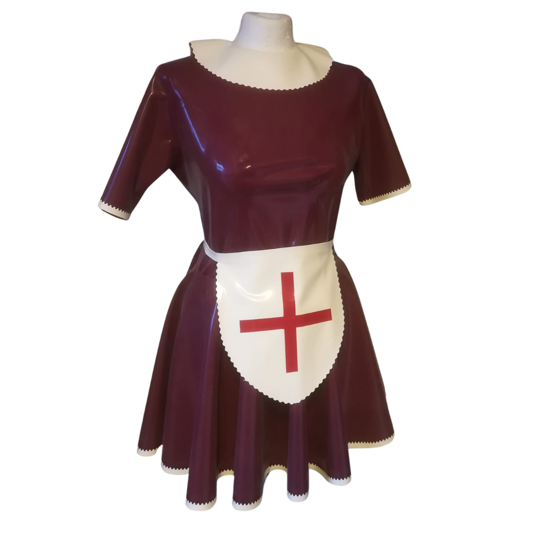 A plum latex swing dress with white wavy trim edging and pan collar. The short sleeve dress has matching white apron and cap with red cross.