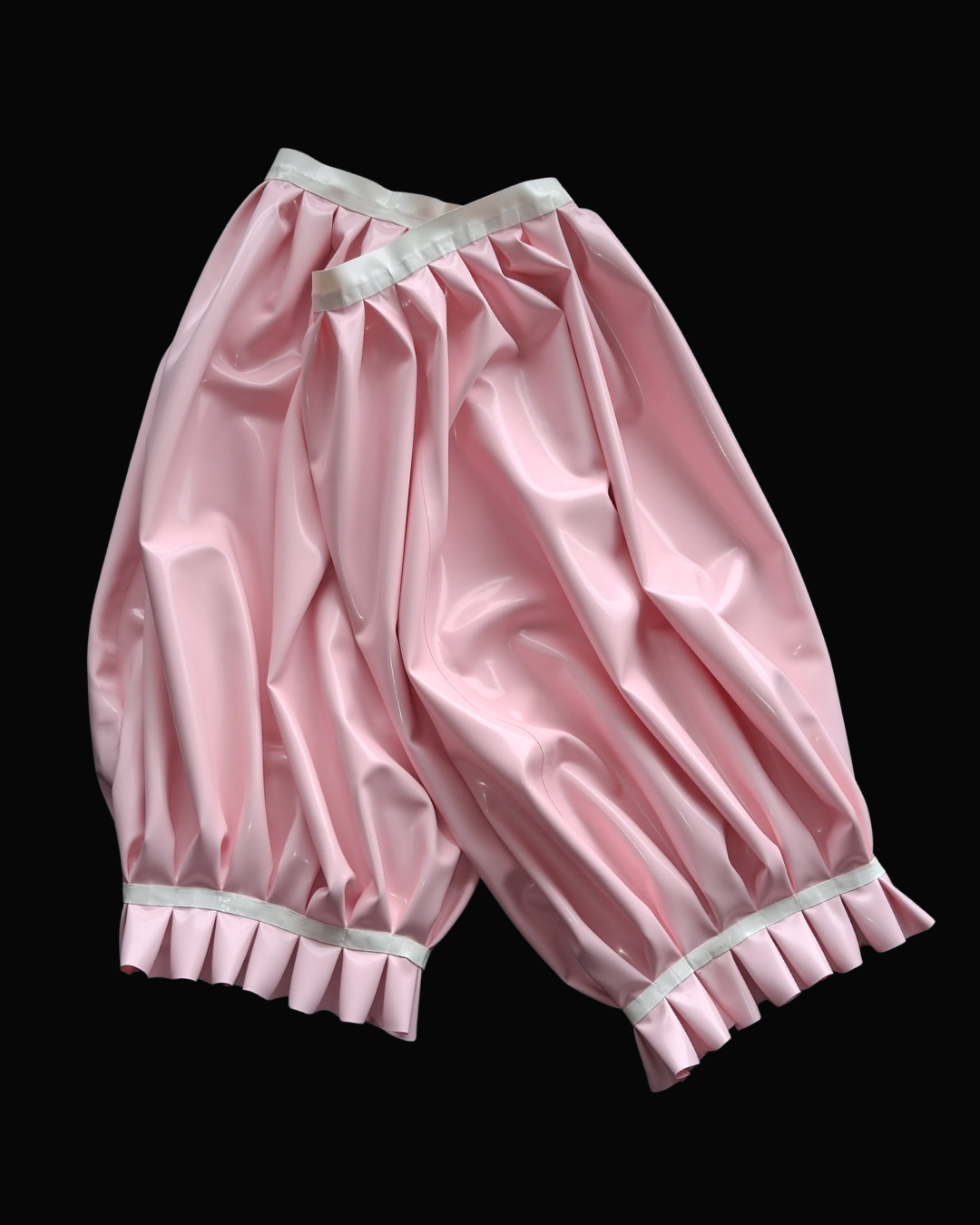 A pair of shiny light pink latex bloomers with white trim at the waistband and cuffs, shown against a solid black background.