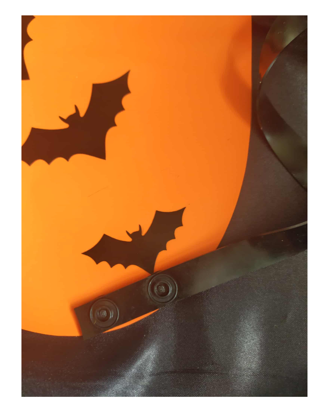 Close-up of a Halloween apron featuring a large orange circle with black bat cut-outs and a black latex bow, set against a dark background.