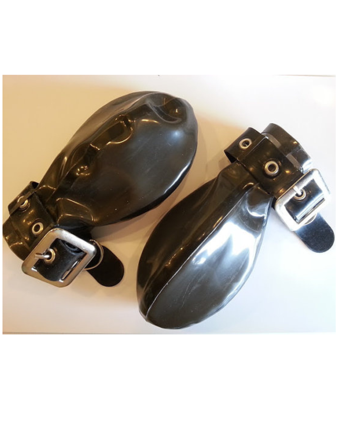 Two glossy black rubber ball mitts with adjustable black straps and silver metal buckles, shown on a plain light background.