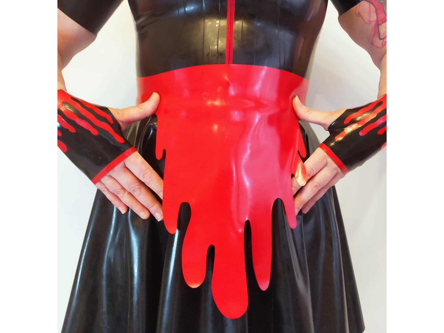 Person wearing a black latex outfit with red blood-like latex apron on a white background