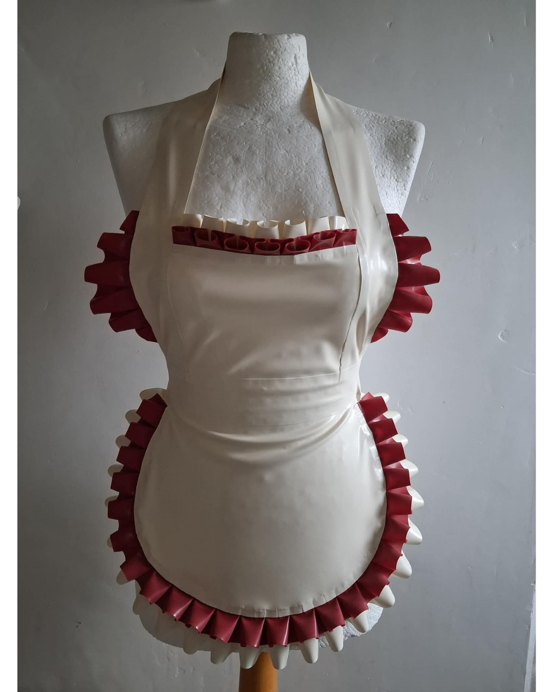 White apron with red ruffled trim on a mannequin against a plain background