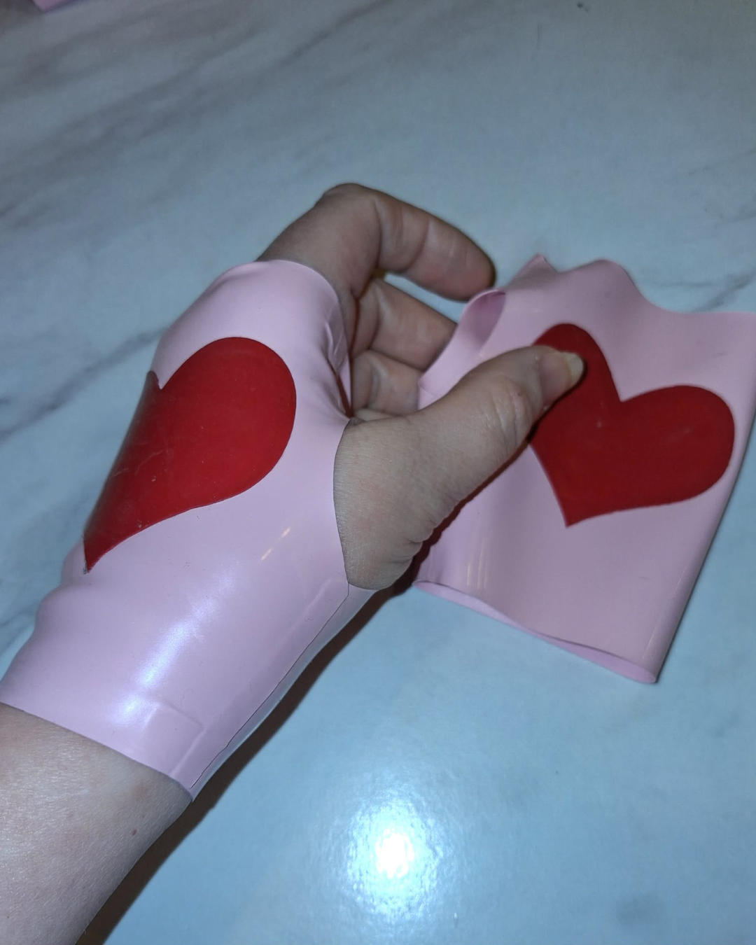 Hand wearing pink latex gloves with red heart designs on a light background