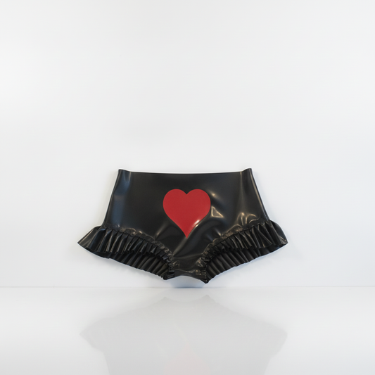 Black latex high-waisted knickers with a red heart graphic on the front and a ruffled hem, displayed on a white reflective surface.
