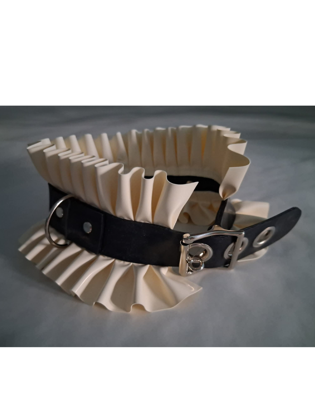 Cream-colored ruffled latex collar with black latex strap on a gray background
