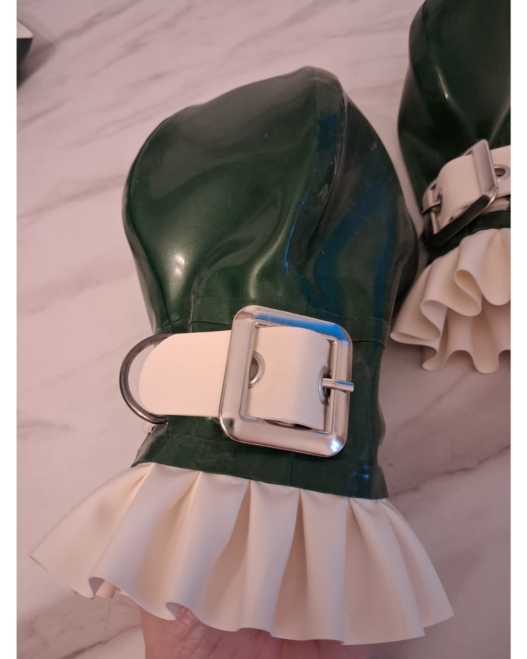 A pair of metallic green latex ball mitts with white frill details.