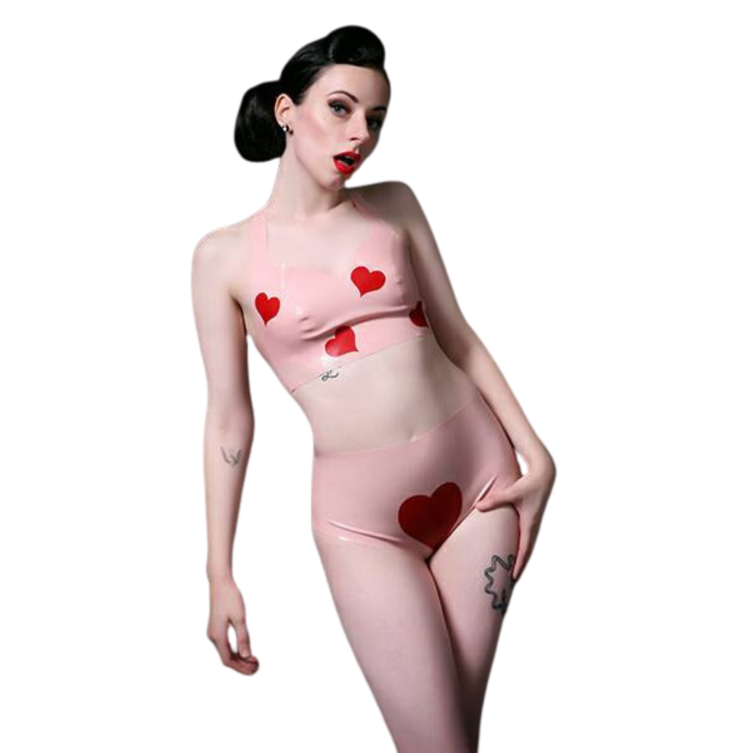 A pale pink two piece latex under wear set. The outfit includes a crop top and a pair of high rise pants. The top features four red heart appliques. The pants have one large red heart on the front.